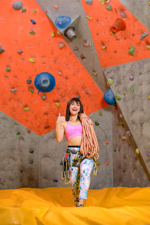 Young Smiling Woman Climber with Rope and Carbines in Climbing Gym. Extreme Sport and Indoor Climbing Conceptの写真素材