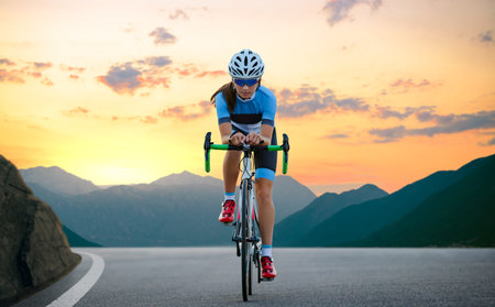 Woman Cyclist Riding Road Bike in the Beautiful Mountains at Sunset. Adventure, Healthy Lifestyle, Sportの写真素材
