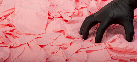 Hand in new black latex medical glove on background of a lot pink rubber glovesの写真素材