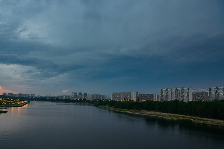 Cityscape with thunderstorm over apartments buildings and large river at foreground at duskの写真素材
