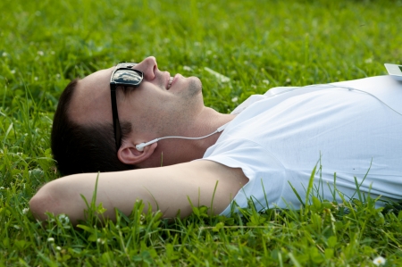 Man lie on the grass with tablet in the park and listening to musicの写真素材
