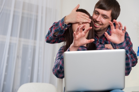 Portrait of young couple using laptop at home. Man close eyes his womanの写真素材