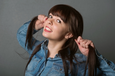 Portrait of young pretty cute girl holding her brown hairs on grayの写真素材
