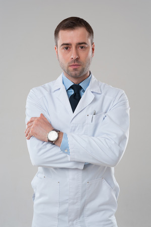 Portrait of serious doctor mature male with crossed arms isolated on grey backgroundの写真素材