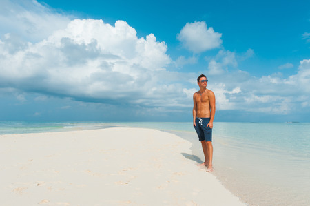 Attractive man looks around standing on beautiful beach with white sand and blue indian ocean. Summertime holidays at paradise place at Maldivesの写真素材