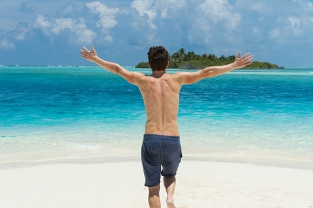 Man running with his hands up on the beach on backgound of island in the oceanの写真素材
