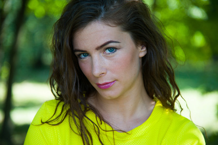 Beautiful portrait of woman with long hairs in yellow bright t-shirt in park, nature background of treesの写真素材