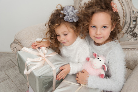 Two pretty cute child girls with gifts on coach at Christmas timeの写真素材