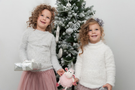 Two cute girls with sheep toy and gifts near Christmas tree on white backgroundの写真素材