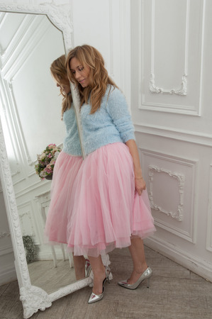 Beautiful blonde woman in pink skirt and silver shoes in classical interiorの写真素材