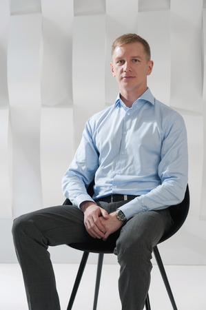 Business man sits on chair against background of abstract modern urban interiorの写真素材
