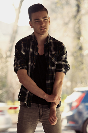Handsome fashion young man walk on street in city. Background of park treesの写真素材