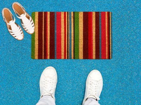 Beautiful Colorful Vertical striped Printed Welcome zute doormat placed with Shoes and Sandles placed on concrete floorの写真素材