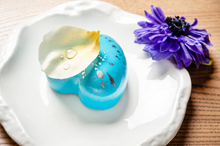 Blue mousse cake on white plate with flower and petals.の写真素材