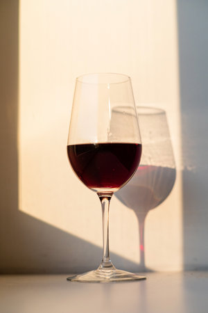 Glass of red wine on a white table with sunlight in the backgroundの写真素材
