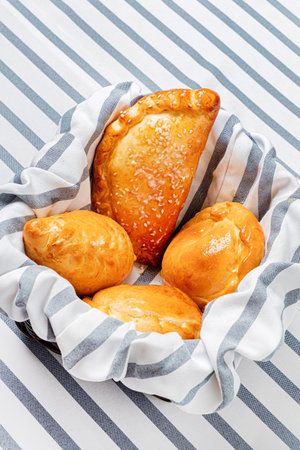 Pies with sesame seeds in a basket on a striped tablecloth