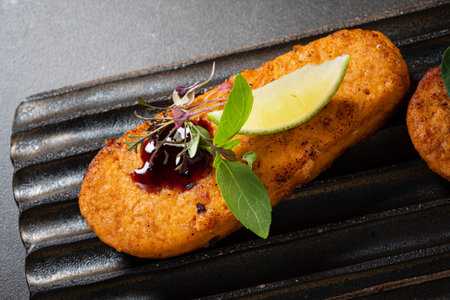 A mouthwatering dish featuring a golden-brown savory treat, elegantly garnished with a slice of lime...