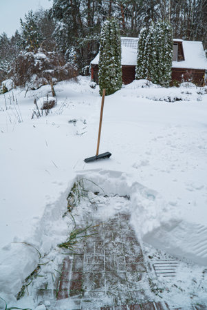 A heavy blanket of snow envelops the ground, creating a picturesque winter wonderland. A shovel stands upright, marking the spot where the path has been cleared, revealing the cabin nearby.の写真素材