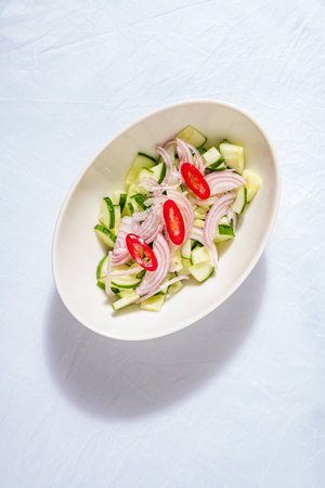 Crisp cucumber pieces intermingle with thin slices of red onion and juicy tomato in a bowl, creating a refreshing dish perfect for warm weather. The vibrant colors invite a tasty experience.の写真素材