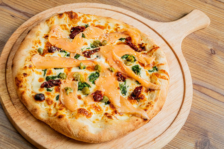 Savory thin-crust pizza showcases an exquisite blend of toppings including smoked salmon, fresh kale, and drizzled with a rich creamy sauce on a wooden serving board.の写真素材