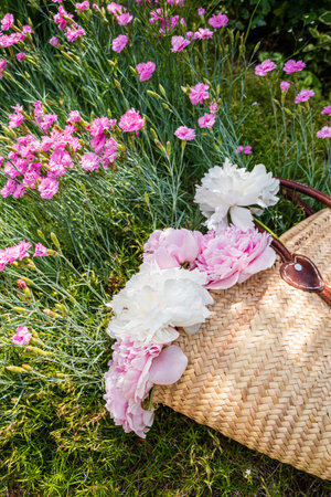 A beautifully arranged basket with peonies rests in a colorful garden filled with flowers.の写真素材