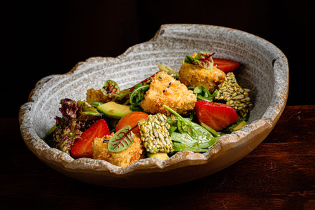 A delightful arrangement of mixed greens, crispy bites, and fresh strawberries awaits savoring.の写真素材