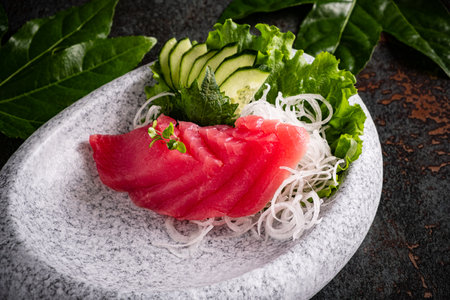 Slices of vibrant sashimi arranged beautifully with fresh greens and cucumbers.の写真素材