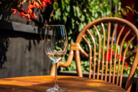 A delicate wine glass stands on a wooden table, surrounded by vibrant greenery and blooming flowers.の写真素材