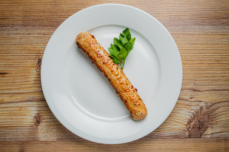A perfectly grilled sausage rests on a pristine white plate, accented by fresh parsley.の写真素材