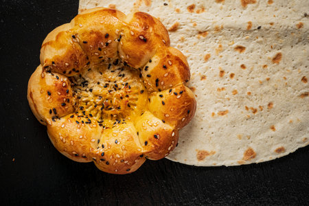 A golden sesame-topped bun rests beside flatbread on a textured surface.