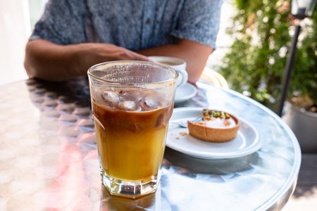 Iced coffee sits on a table next to a delicious pastry, while someone enjoys the casual atmosphere.