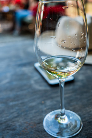 A refreshing glass of white wine rests on a wooden table, droplets glistening in the sunlight.の写真素材