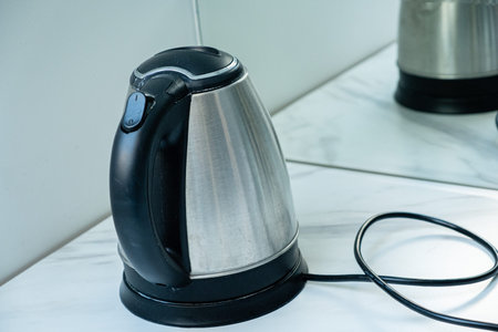 A shiny electric kettle sits on a marble countertop, reflecting light while waiting for use.