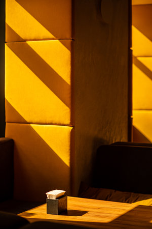 Soft shadows across a wooden table in a tranquil cafÃ©, where sunlight bathes the walls in warmth.の写真素材