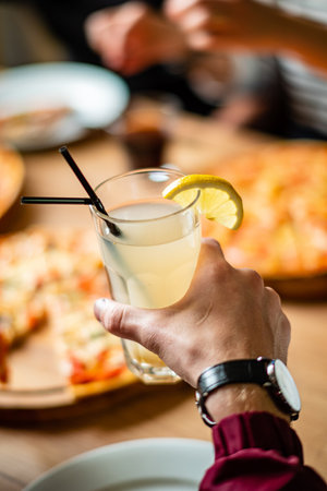 Hands raise a chilled beverage with lemon beside a delicious pizza feast, celebrating togetherness.の写真素材