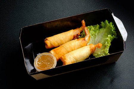 Three golden shrimp spring rolls rest alongside a cup of dipping sauce and fresh lettuce.の写真素材