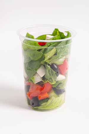 A vibrant salad with spinach, tomatoes, peppers, and olives in a clear container.の写真素材
