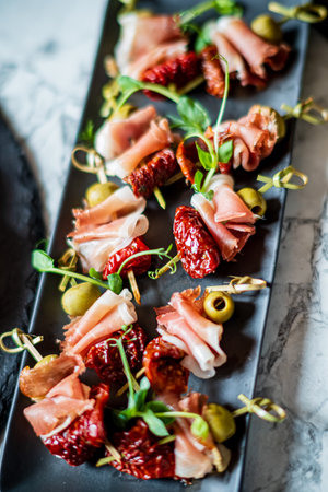Cured meats and olives are artfully displayed on skewers, ready to delight guests at a gathering.の写真素材