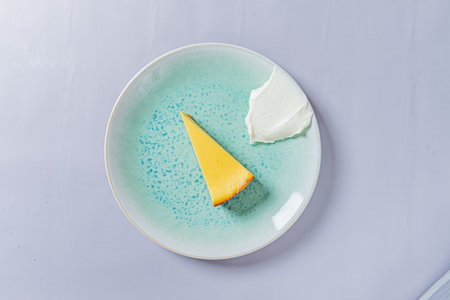 A vibrant cheesecake slice sits next to a creamy dollop, making a delightful dessert.