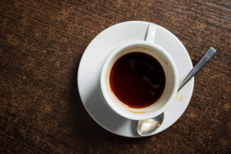 A small cup filled with dark coffee sits on a rustic wooden table, inviting warmth and comfort.
