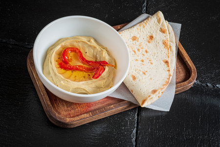 Rich roasted red pepper hummus drizzled with oil, served with warm flatbread on a tray.の写真素材