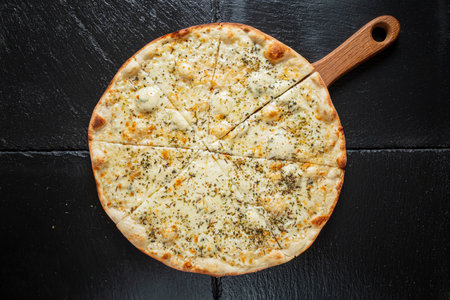 A freshly baked white pizza topped with herbs lies on a wooden paddle, inviting a tasty feast.の写真素材