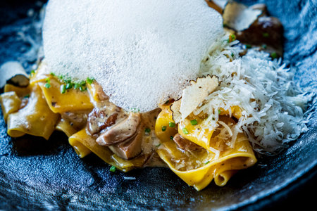 A beautifully crafted pasta topped with creamy foam, cheese, and herbs showcases culinary art.