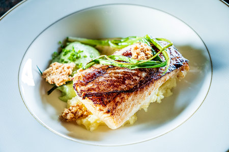 A beautifully presented grilled fish fillet on creamy mashed potatoes, accented with fresh greens.