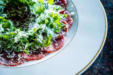 A beautifully arranged plate featuring thinly sliced carpaccio, topped with fresh greens and cheese.の写真素材