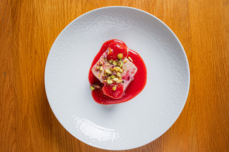 A curated dessert on a white plate, topped with raspberry sauce and pistachios.