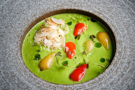 A vibrant green soup showcases colorful vegetables and sliced almonds, inviting taste and elegance.の写真素材
