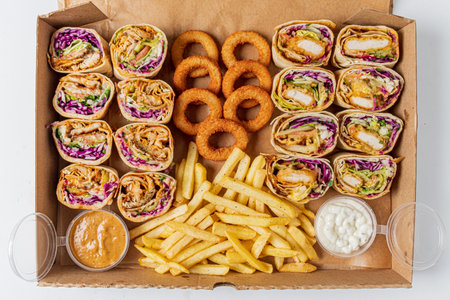 A mouthwatering assortment of chicken wraps, crispy onion rings, and golden fries on display.の写真素材