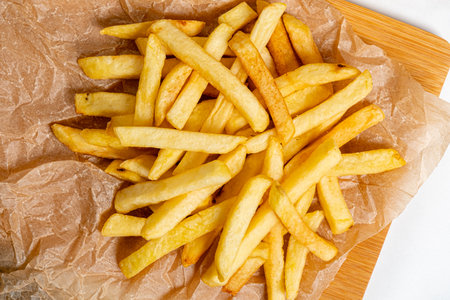 Golden crispy fries piled on parchment paper evoke warmth and comfort, perfect for sharing.の写真素材