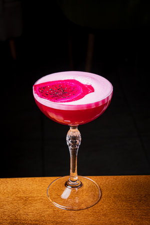 An alluring cocktail featuring a vibrant dragon fruit slice on top, captivating in low light.の写真素材